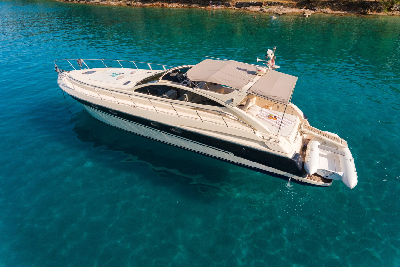 Aerial view of a dark-hulled motor yacht under way in clear turquoise water off the Dalmatian coast, tender stowed aft.