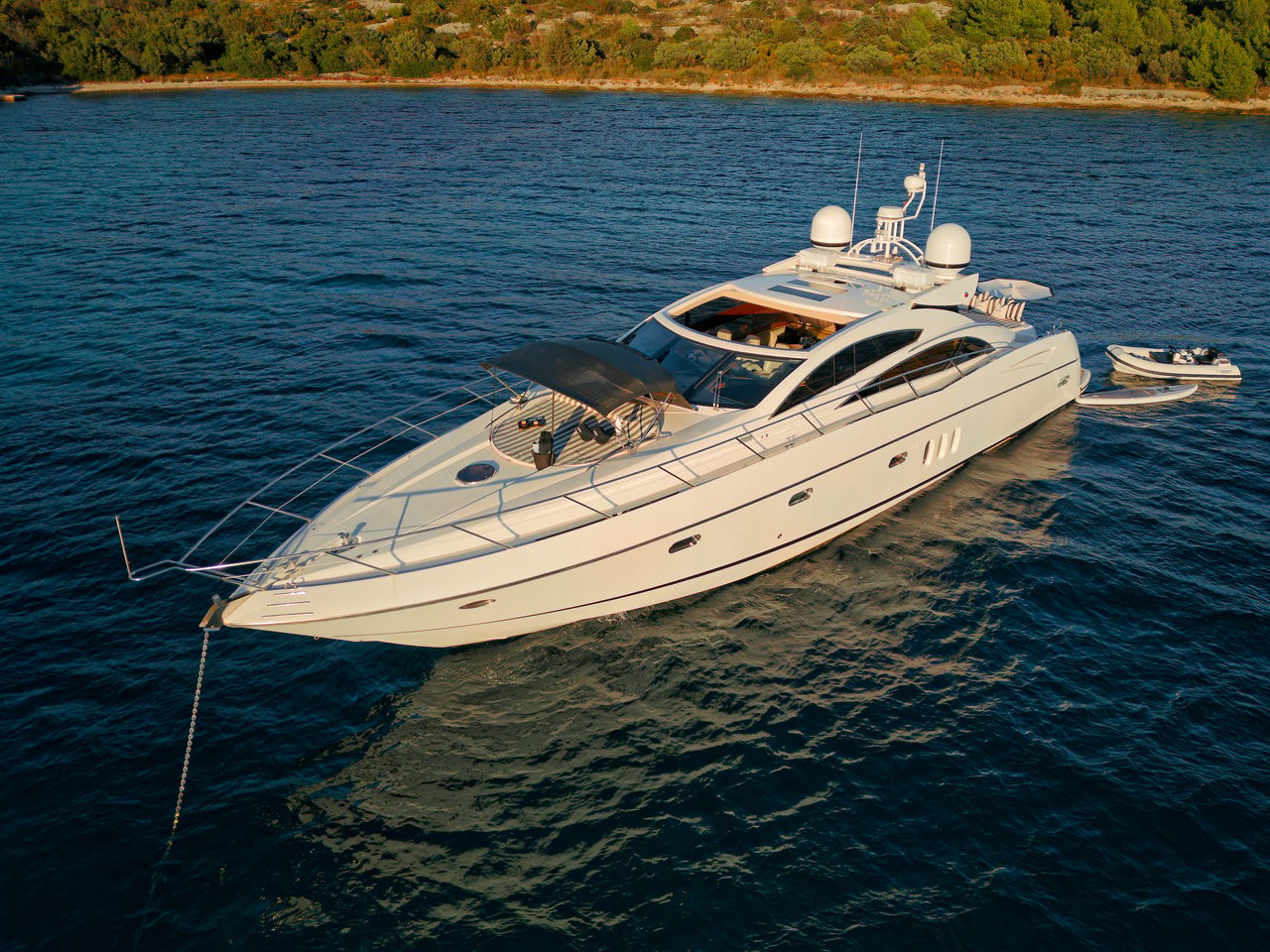 Aerial view of a crewed motor yacht lying at anchor in deep blue water off the Dalmatian coast near Split, with a tender alongside.